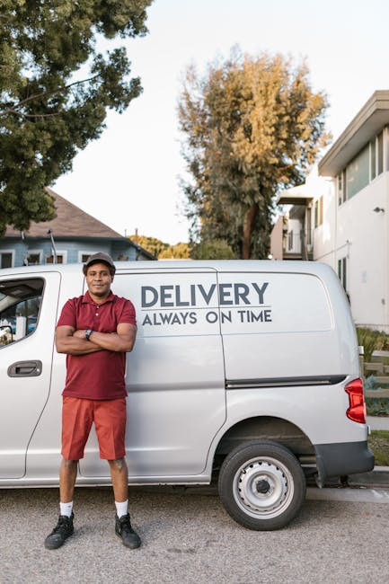 A man with dark curly hair, wearing a dark grey cap and a maroon polo shirt, stands outdoors next to a white delivery van with the words 'DELIVERY ALWAYS ON TIME' printed on the side. He is smiling an